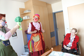 Zwei Clinic Clowns stehen am Bett in einer Pflegeeinrichtung. 